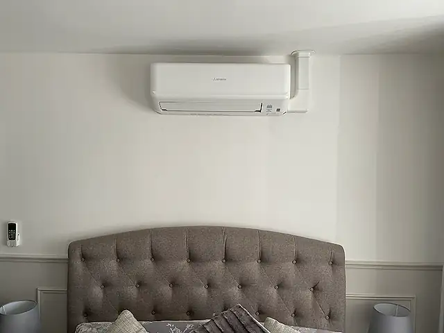 A compact wall-mounted air conditioner above a bed, the kind of air conditioning we fit for homes in Bethnal Green
