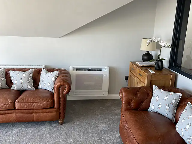 Floor console air conditioning in a lounge, London Floor-standing console air conditioning unit beneath a sloping ceiling in a lounge with leather Chesterfield sofas
