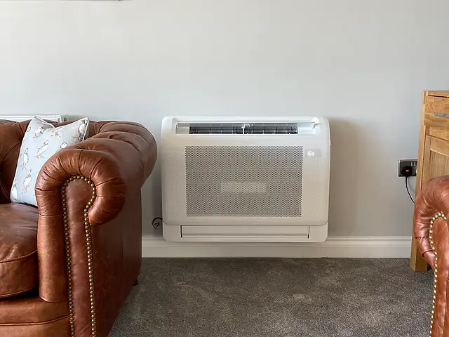 Floor-standing air conditioning console, London Close view of a white floor console air conditioning unit installed at skirting level beside a leather sofa